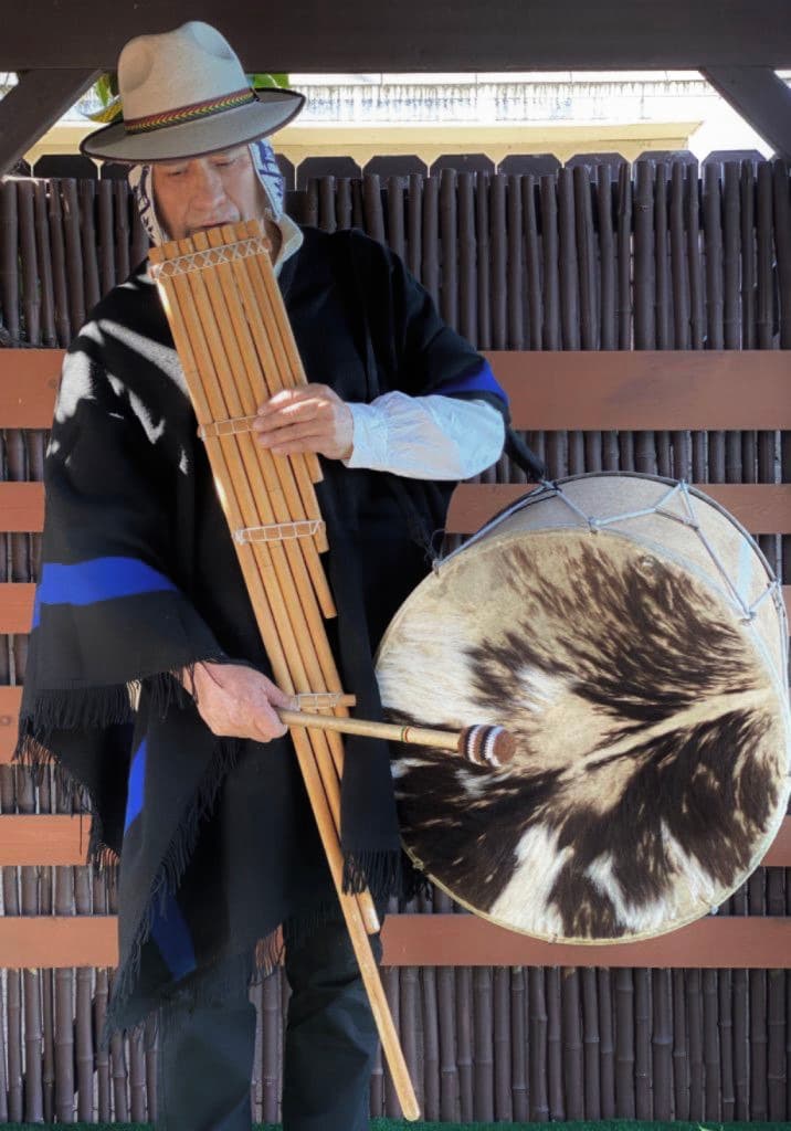 Performer holding siku panpipes and a drum for an Andean music demonstration